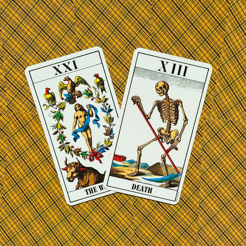 Tarot kortos Rider–Waite stiliaus su baltu rėmeliu, ant geltono raštuoto fono išdėstytos The World ir Death kortos, fotografuota iš viršaus
