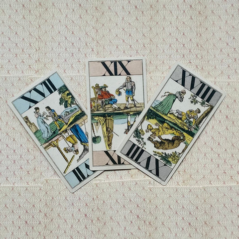 Tarot kortos Rider–Waite stiliaus, trys apverstos kortos fanuotos ant smulkiai raštuoto popierinio fono, matomas variantų išdėstymo kampas