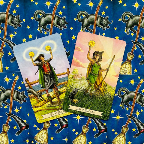 Tarot kortos — Ace of Pentacles ir Two of Pentacles prie mėlyno fono su raganių skrybėlėmis ir šluotomis, kortos persidengia kampu