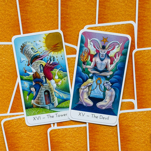 Tarot kortos su atverstu priekiu: artimas planas dviem iliustruotoms kortoms (XV Išdavikas, XVI Bokštas), oranžinė nugarėlė matoma