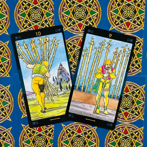 tarot kortos Rider–Waite stiliaus, dviejų kortų išklotinė (10 ir 9 lazdų) ant mėlyno pentaklių fono, iš arti