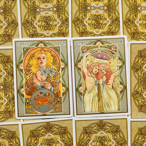 Tarot kortos su Art Nouveau iliustracijomis — dvi atverstos kortos (Vėžys ir Dvyniai) su auksinėmis ornamentuotomis nugarėlėmis