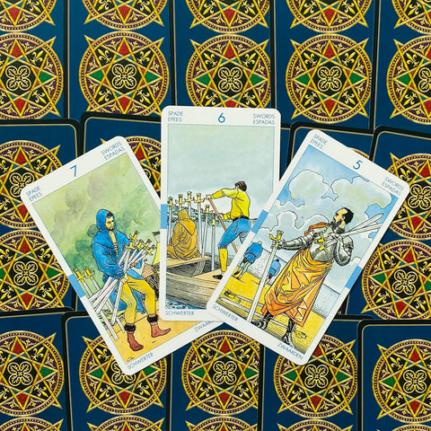 Tarot kortos trijų kardų derinys (5,6,7) iš viršaus ant mėlynos ornamentuotos nugarėlės, skirta trijų kortų išklotai