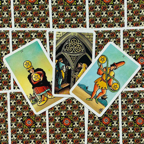 Tarot kortos Rider–Waite stiliaus, trys atviros pentaklių kortos iš viršaus ant ornamentuotos raudono‑juodo nugarėlės, ryškūs spalvoti motyvai