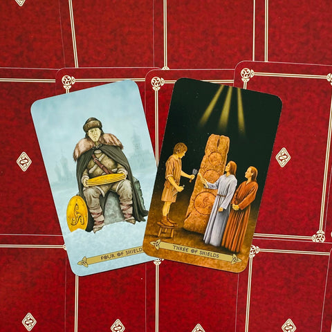 Taro kortos Rider–Waite stiliaus, dvi atverstos kortos (Three of Shields ir Four of Shields) ant raudonos nugarėlės, parodytos iš viršaus, rodantis priekinio meno variantą