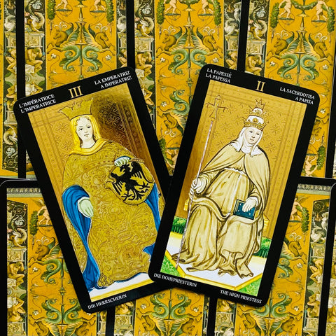 Tarot kortos klasikinės aukso ir juodos spalvų, dvi atverstos Didžiosios Arkos — Imperatorė ir Vyriausioji kunigė.