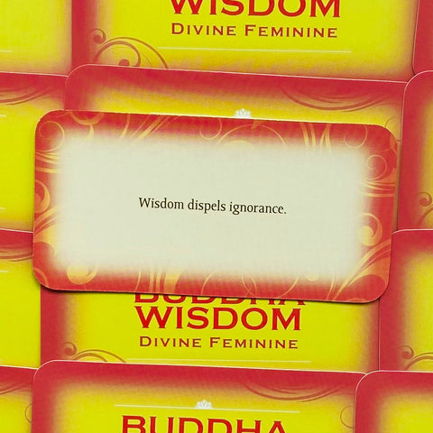 Buddha išminties kortos geltonai-raudonu dėklu, viršuje atidaryta kortelė su tekstu Išmintis išsklaido nežinojimą, artimas kampas