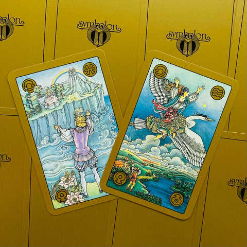 Tarot kortos Symbolon aukso dėkle, dvi spalvingos atverstos kortos diagonaliai ant auksinio fono