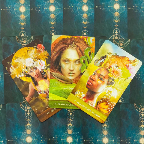 Tarot kortos trijose atverstose kortose su ryškiomis geltonai–žaliomis iliustracijomis ir mėlyna ornamentuota nugarėle