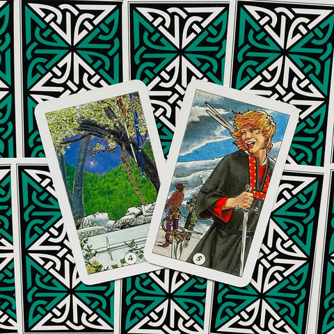 Tarot kortos, dvi atverstos kalavijų kortos ant žaliai–juodo rašto nugarėlių su ryškiomis iliustracijomis