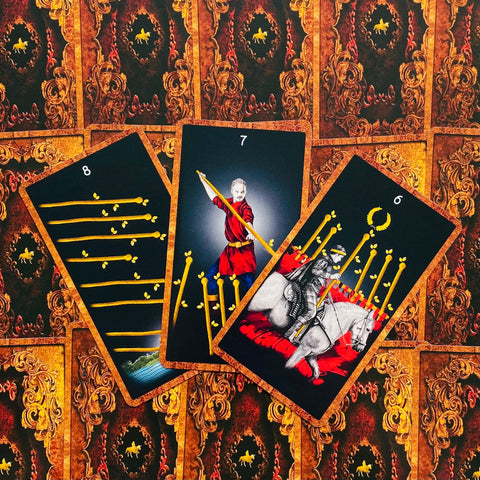 Tarot kortos — trijų kortų rinkinys (8, 7, 6 lazdelės) su juodu fonu, auksinėmis lazdelėmis ir ryškiomis raudonomis detalėmis, ornamentuota nugarėle