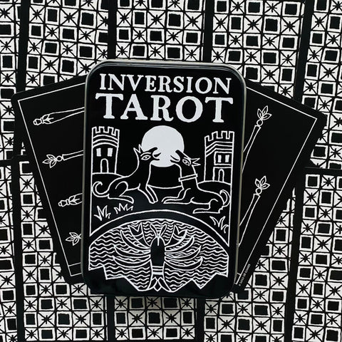 Tarot kortos Inversion juodai baltas rinkinys metalinėje dėžutėje, kortos išskleistos vėduoklė prieš geometrinį foną