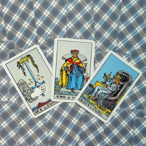 tarot kortos Rider–Waite komplekte — trys atverstos kortos (Ace of Swords, King of Cups, Queen of Cups) ant mėlyno languoto fono, plokščias išplanavimas