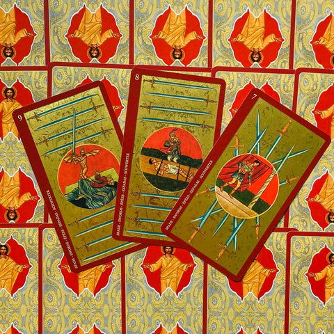tarot kortos su raudonais ir auksiniais nugarėlių raštais, trys kalavijų kortos (7–8–9) iš viršaus išskleistos, skirtingų iliustracijų variantas