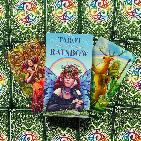 Prekės puslapyje: Tarot at the End of the Rainbow dėžutė priekyje, dvi atverstos spalvotos kortos kampu ant žalio raštuoto fono
