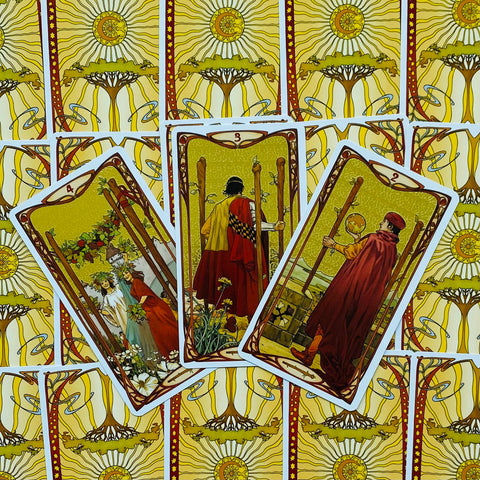 Tarot kortos su geltona saulės nugarėle, trys atverstos Lazdų kortos centre ir ornamentuota fono rašto kompozicija