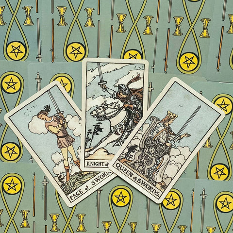 Tarot kortos Rider–Waite trijų kardų išklotė (Page, Knight, Queen) ant žalių pentaklių nugarėlių, fokusas į kardų simboliką ir priekinį kampą