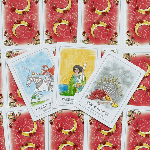 Tarot kortos su raudona gėlių ir mėnulio nugarėle, trys atverstos kortos (Riteris, Puslapis, Dešimt kalavijų) centre
