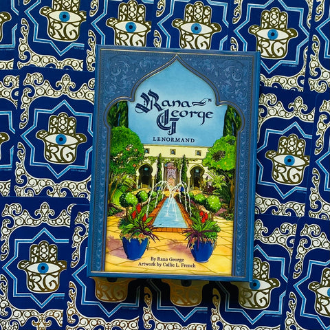 Lenormand kortų rinkinys Rana George mėlyname, auksu ornamentuotame dėkle, padėtas ant ryškaus mėlyno Hamsa rašto fono