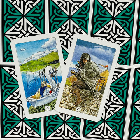 Tarot kortos Rider–Waite stiliaus, dvi atviros kortos (6 ir 7 kardai) ant žaliai–juodo ornamentuoto galinio dizaino fono
