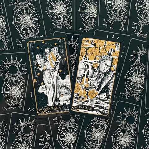 Tarot kortos juodos ir auksinės, artimas kadras su dviem atverstomis kortomis — Queen of Air ir Page of Air ant dekoratyvių nugarėlių