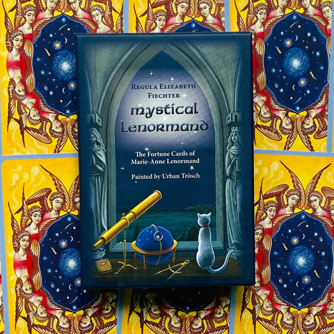 Lenormand kortos Mystical, tamsiai mėlynas dėklas su teleskopu ir katės iliustracija ant spalvingo angeliško fono