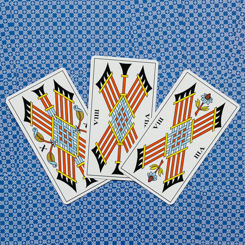 Tarot kortos trys lazdų kortos fanuotos, ryškūs oranžiniai ir mėlyni motyvai ant mėlyno raštuoto fono