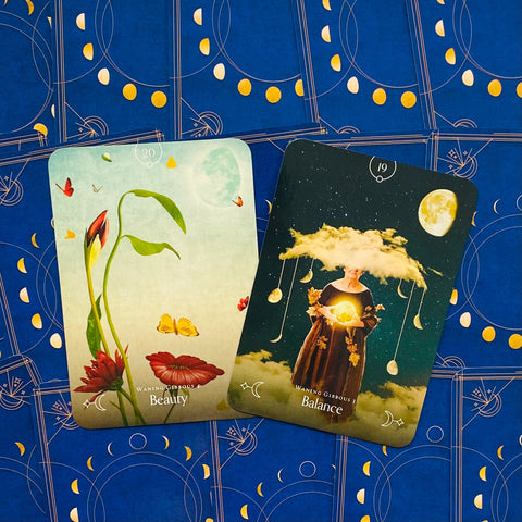 Tarot kortos dvi atverstos kortos — "Beauty" su raudonomis gėlėmis ir drugeliais bei "Balance" su figūra ir mėnuliu ant mėlyno dekoratyvaus fono