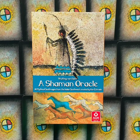 Orakulų kortos A Shaman Oracle, centrinis viršelis su šamanų plunksnuota galvos puošmena, mėlyna pavadinimo juosta ir AGM logotipu