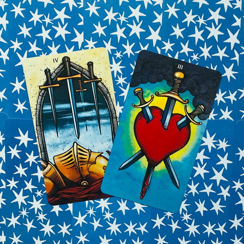 Tarot kortos Rider–Waite, dvi atverstos kortos (Trys kardai, Keturi kardai) ant mėlyno žvaigždėto fono, artimas kampas