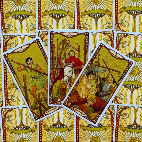 Tarot kortos, Art Nouveau iliustracijos ir aukso‑geltonės nugarėlės; trijų atverstų lazdų kortų fanas, artimas kadras