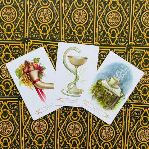 Tarot kortos trijų kortų kompozicija iš viršaus: atverstos Temperance, Cornucopia ir Rest ant žaliai auksinės nugarėlės