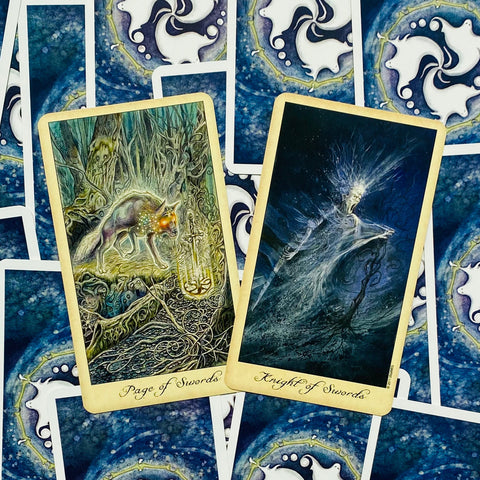 Tarot kortos su auksiniu kraštu, dvi atviros kortos (Page of Swords, Knight of Swords) ant mėlyno nugarėlių fono, arti apžvalgai