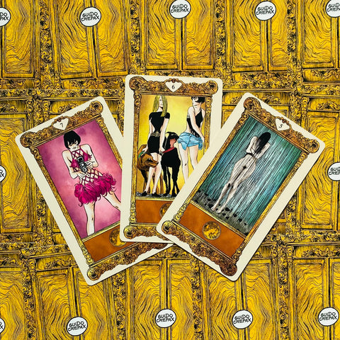 tarot kortos Guido Crepax — trys atverstos kortos su figūromis ant geltono, ornamentuoto nugarėlės fono