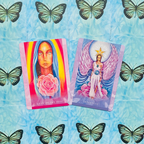 tarot kortos rožinė Lady of the Rose ir violetinė Intention, atverstos ant mėlyno fono su drugeliais, matomos priekio iliustracijos