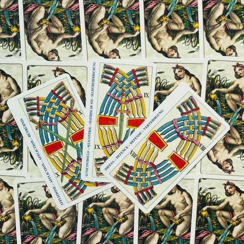 tarot kortos spalvotais vytelių raštais, trys išskleistos kortos centre ant stovinių iliustruotų nugarėlių