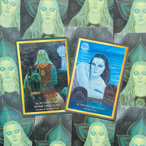 Orakulo kortos su auksinėmis kraštinėmis — dvi atverstos kortos (Activate the Divine Masculine ir Transformation) mėlyno‑žalsvo tono, plokščias produkto išdėstymas, matomas priekinis dizainas