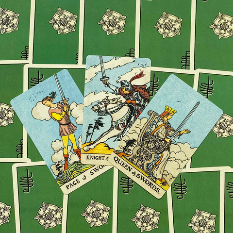 Tarot kortos atvertos ir išdėstytos fanuotos — Page, Riteris ir Karalienė kardų matomos ant žalių nugarėlių