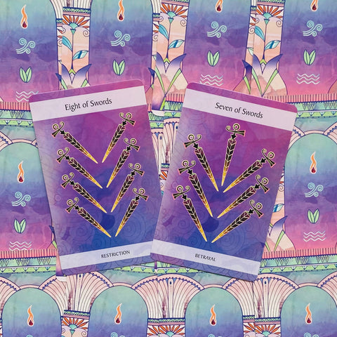 tarot kortos dvi atverstos violetinės kardų kortos (Eight of Swords ir Seven of Swords) su auksinėmis detalėmis ant dekoratyvios fono drobės