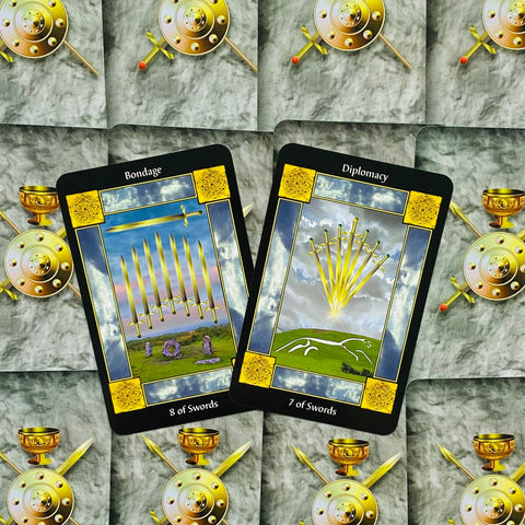 Tarot kortos juodais kraštais su auksinėmis detalėmis, 8 ir 7 kardų porinė išklotinė ant skydų ir taurių motyvo fono
