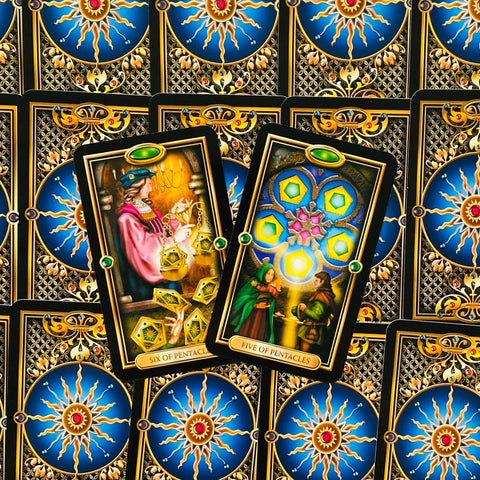 Tarot kortos prabangiais mėlynais ir auksiniais nugarėlių raštais, dvi atvertos kortos (6 ir 5 pentaklų) persidengiančios kampu