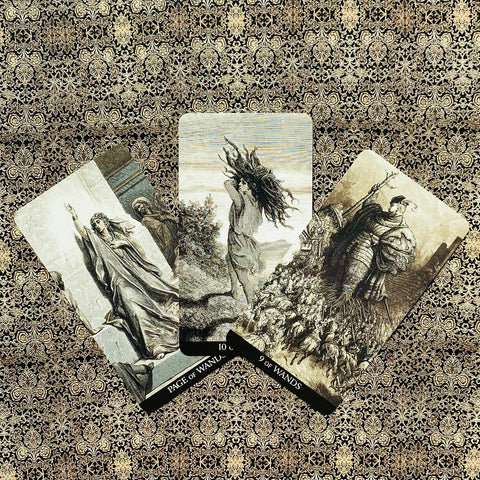 Tarot kortos su retro juodai rudos iliustracijomis, trijų kortų pavyzdinis išdėstymas ant auksinio ornamentuoto audinio