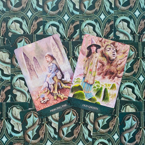 tarot kortos iliustruotos, dvi atvertos kortos kampu ant žalsvos drakoninės nugarėlės fono, akcentas ant pastelines moters sėdinčios ir stovinčios figūros bei samanotų akmenų