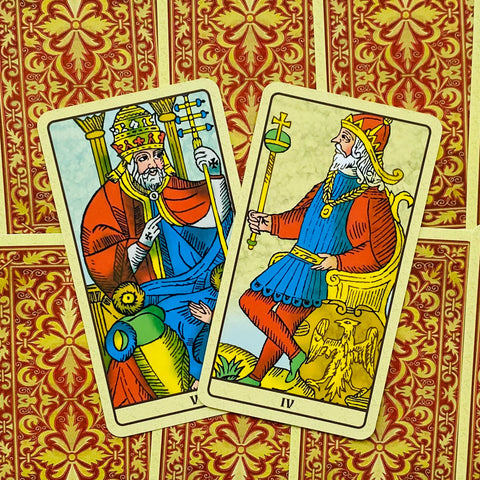 Tarot kortos Rider–Waite stiliaus, dvi kortos (V Popiežius ir IV Imperatorius) padėtos kampu ant raudonai auksinės nugarėlės