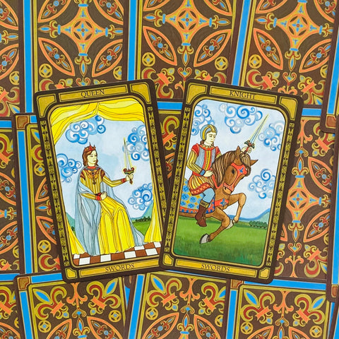 Tarot kortos su atvertomis Kardų karalienės ir Riterio kortomis, ryškiai geltonos ir mėlynos iliustracijos bei ornamentuotos nugarėlės