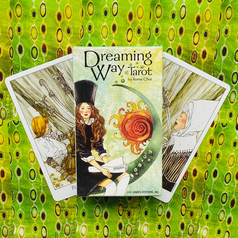 Dreaming Way Tarot dėžutė centre ant ryškaus žalsvo fono, priekyje iliustruota dangaus moters figūra ir dvi išskleistos kortos šonuose, parodytas dėžutės priekinis vaizdas ir kortų kampai
