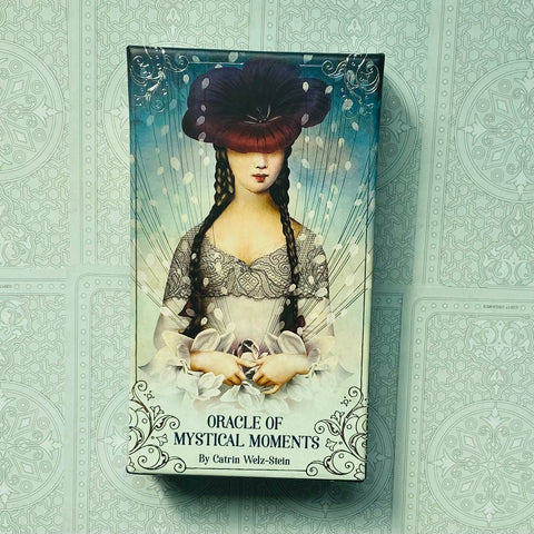 Orakulo kortos Oracle of Mystical Moments dėžutės priekis su stilizuota moters iliustracija, pasteliniai mėlyni ir smėlio tonai, aut. Catrin Welz‑Stein