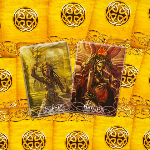 tarot kortos — dviejų kortų priekiniai variantai: Hekate (Illumination) ir Hathor (Contentment), artimas planas su auksiniais nugarėlės raštais, produkto detalė