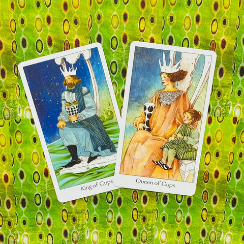 Tarot kortos — dvi kortos (Karalius ir Karalienė Taurų) atverstos ant žalsvo raštuoto audinio kampu, detalė