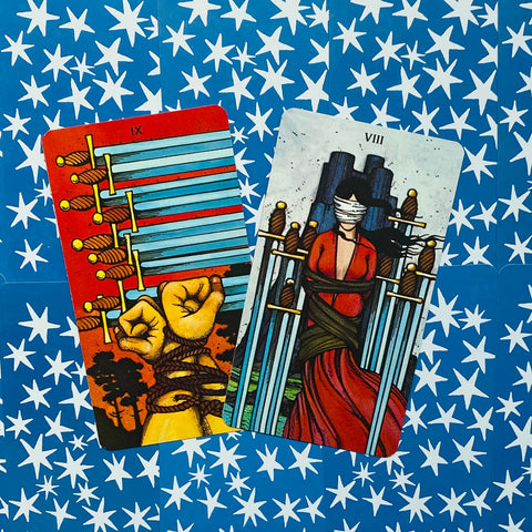 Tarot kortos, dvi įstrižai atvertos spalvotos kortos — kumščiai su virvėmis ir pririšta moteris, mėlynas žvaigždėtas fonas